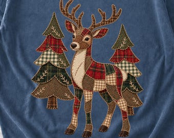 May include: A blue sweatshirt featuring a graphic of a deer and two pine trees. The deer and trees are composed of various patchwork patterns in shades of red, green, brown, and cream, with visible stitching details throughout the design.