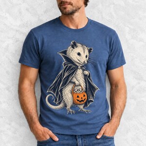 Etched pen illustration of an opossum in a vampire cape holding a candy pumpkin, bone white with orange accent