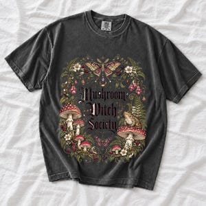 Blackletter text "Mushroom Witch Society" framed by fly agaric mushrooms, ferns and a toad on a mushroom cap