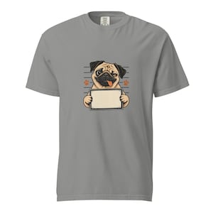 Pode incluir: Uma t-shirt cinzenta de manga curta com o gráfico de um pug bege com cara preta, a piscar o olho e a mostrar a língua. O pug segura uma placa retangular em branco com uma borda preta sobre um fundo de linhas horizontais.