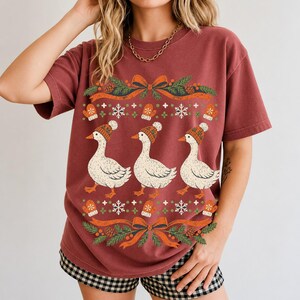 Three geese in pompom knit beanies with mittens, snowflakes and pine borders, retro winter t-shirt graphic