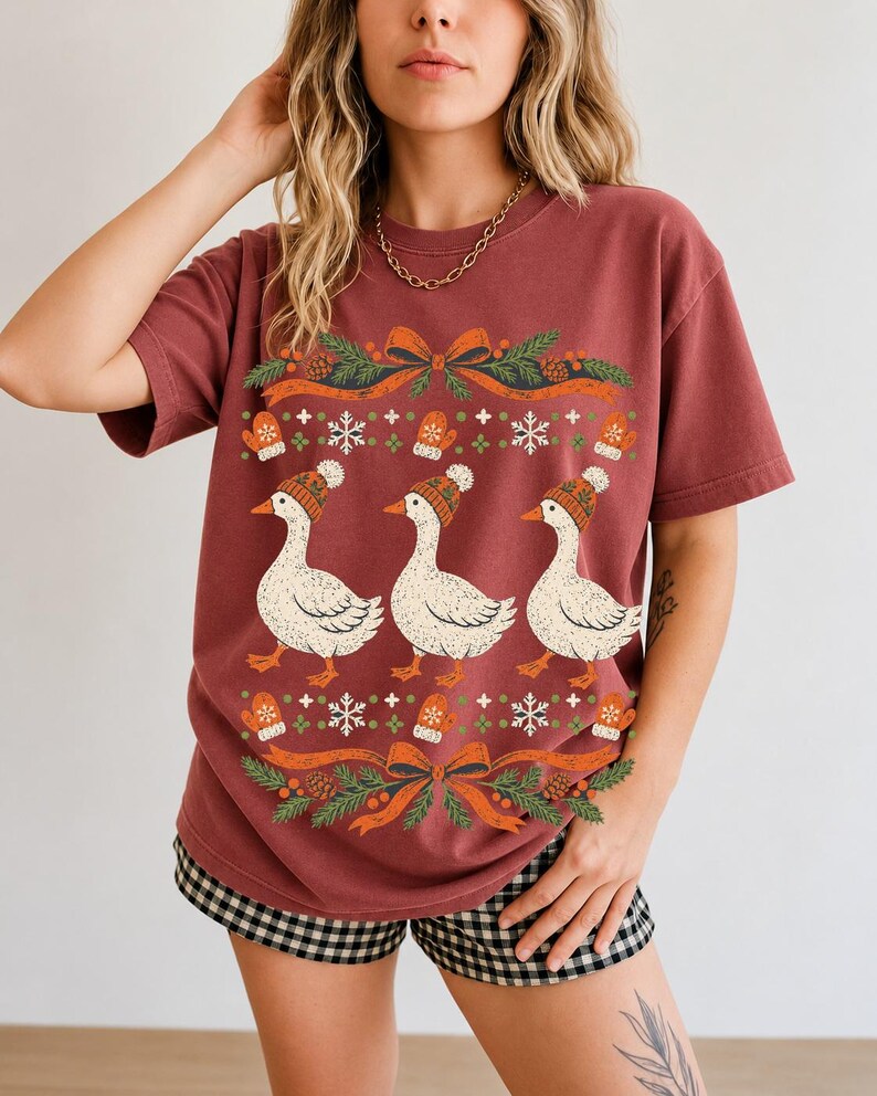 Three geese in pompom knit beanies with mittens, snowflakes and pine borders, retro winter t-shirt graphic
