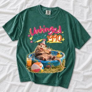 Opossum in party hat in a kiddie pool with cake, 90s film photo style, text "Unhinged Since 1990"
