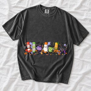 Seven glue sticks and paint pots with faces in Halloween costumes marching past pumpkins and cobwebs