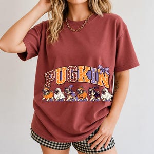 Six pugs in pumpkin, ghost and witch costumes under the arched word PUGKIN, lavender and orange polka-dot varsity style