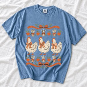 Three fluffy hens with gingham bows between apple and wheat borders, retro folk art fall t-shirt design