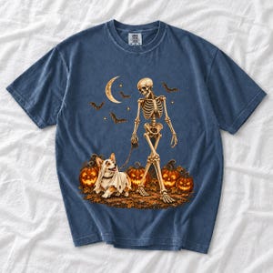 A skeleton walking a corgi in a ghost costume past carved pumpkins under a crescent moon