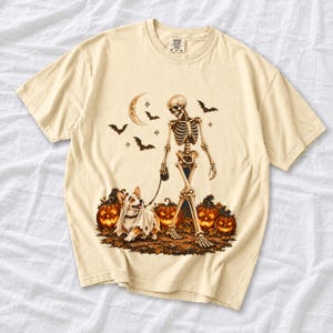 A skeleton walking a corgi in a ghost costume past carved pumpkins under a crescent moon