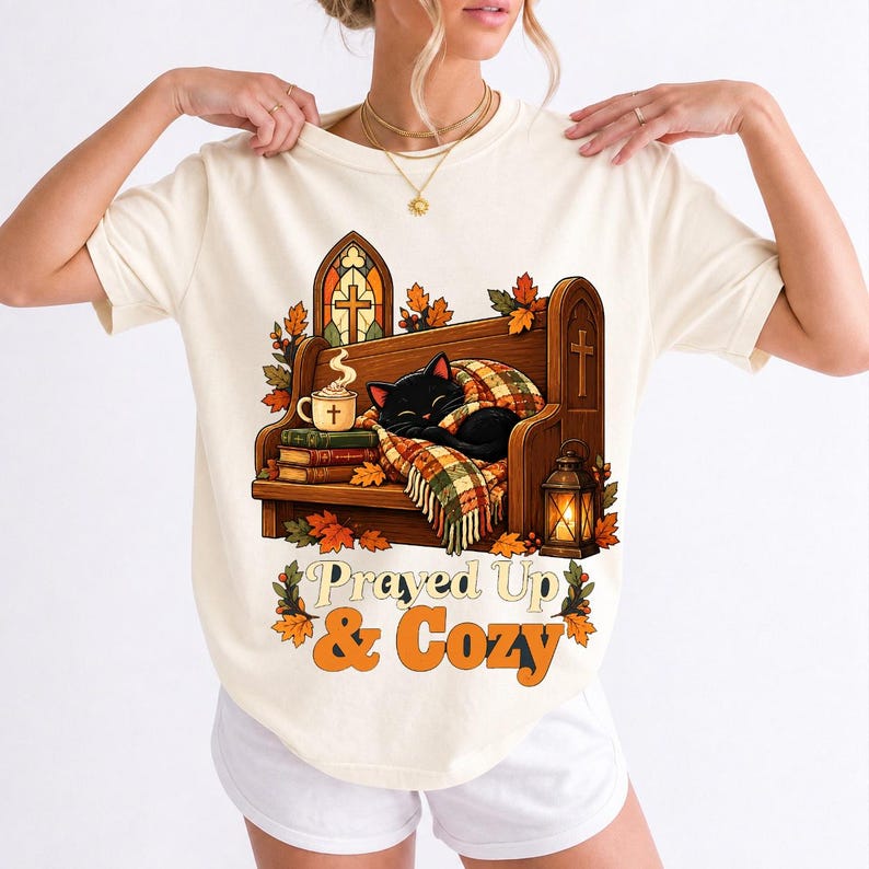 Black cat curled on a church pew with blanket and cocoa among autumn leaves, text "Prayed Up & Cozy", retro illustration