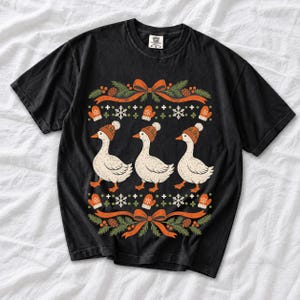 Three geese in pompom knit beanies with mittens, snowflakes and pine borders, retro winter t-shirt graphic