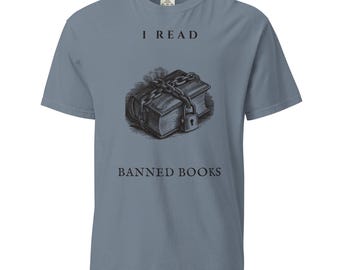 Puede incluir: Una camiseta de manga corta color azul pizarra con un gráfico negro de un libro envuelto en cadenas con un candado. El texto "I READ" aparece sobre el libro y "BANNED BOOKS" debajo, ambos en una tipografía oscura con remates.