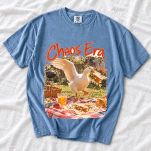 Goose stealing a sandwich from a picnic blanket, 90s film photo style, text "Chaos Era"