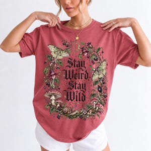 Victorian-style wreath of nightshade, luna moths and toadstools around the words "Stay Weird, Stay Wild"
