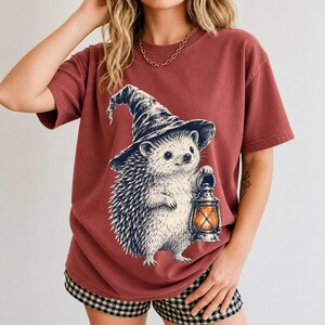 Etched pen illustration of a hedgehog in a witch hat holding a lantern, bone white with orange accent