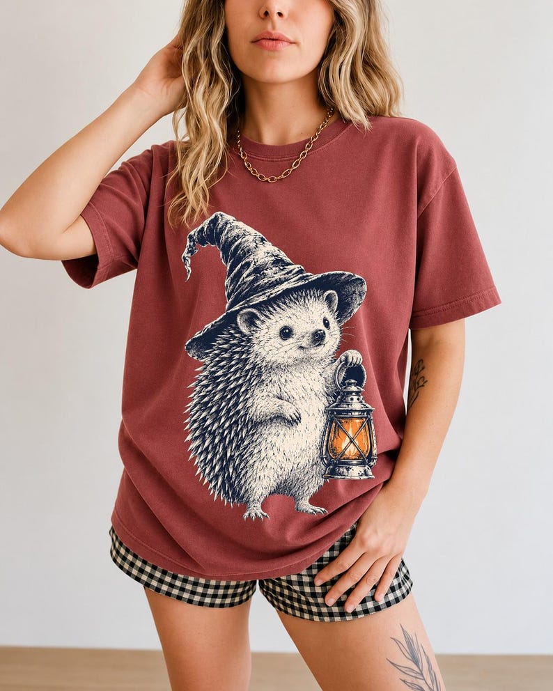 Etched pen illustration of a hedgehog in a witch hat holding a lantern, bone white with orange accent