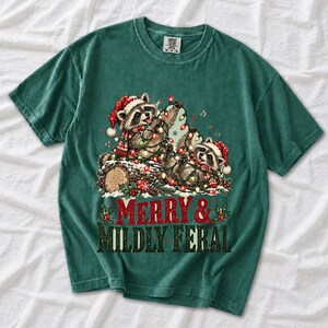 Two raccoons tangled in Christmas lights beside a log with the text Merry & Mildly Feral