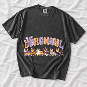 Six corgis in Halloween costumes walking under the arched word CORGHOUL, lavender and orange polka-dot varsity style