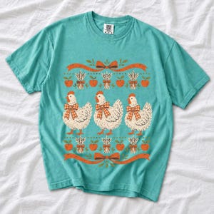 Three fluffy hens with gingham bows between apple and wheat borders, retro folk art fall t-shirt design
