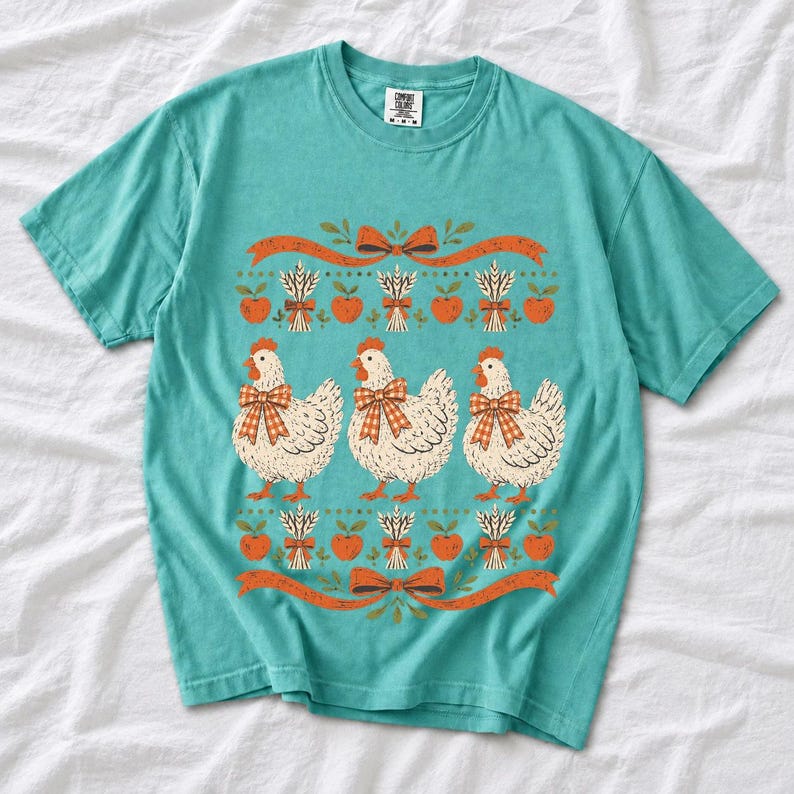 Three fluffy hens with gingham bows between apple and wheat borders, retro folk art fall t-shirt design