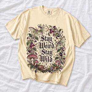 Victorian-style wreath of nightshade, luna moths and toadstools around the words "Stay Weird, Stay Wild"