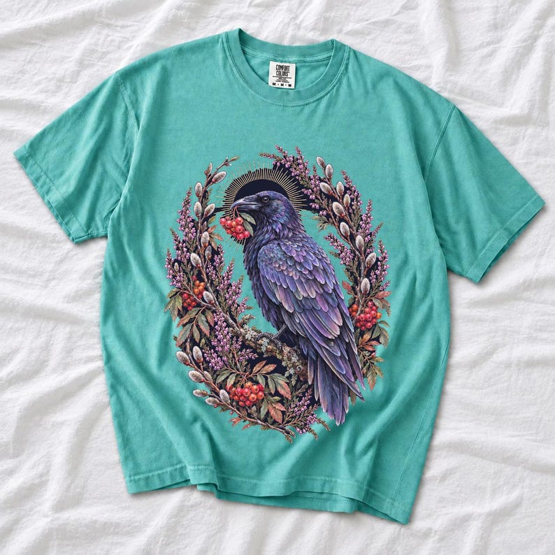 Raven holding a rowan berry inside an oval wreath of heather and catkins, painted cottagecore bird illustration