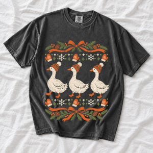 Three geese in pompom knit beanies with mittens, snowflakes and pine borders, retro winter t-shirt graphic