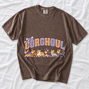 Six corgis in Halloween costumes walking under the arched word CORGHOUL, lavender and orange polka-dot varsity style