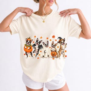 Five watercolor Boston terriers in Halloween costumes with falling autumn leaves