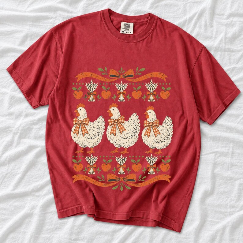 Three fluffy hens with gingham bows between apple and wheat borders, retro folk art fall t-shirt design