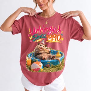 Opossum in party hat in a kiddie pool with cake, 90s film photo style, text "Unhinged Since 1990"