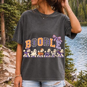 Six poodles in Halloween costumes walking under the arched word BOODLE, lavender and orange polka-dot varsity style