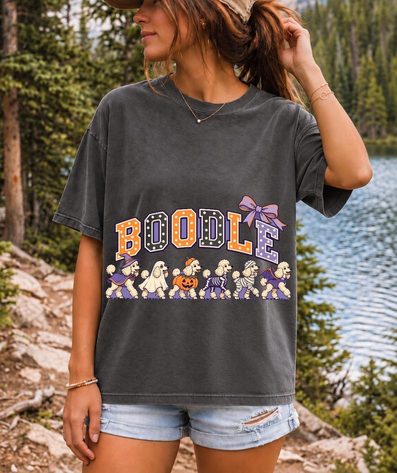 Six poodles in Halloween costumes walking under the arched word BOODLE, lavender and orange polka-dot varsity style