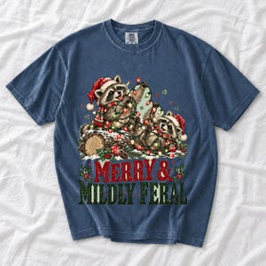 Two raccoons tangled in Christmas lights beside a log with the text Merry & Mildly Feral