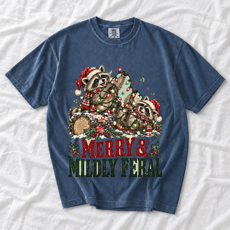 Two raccoons tangled in Christmas lights beside a log with the text Merry & Mildly Feral