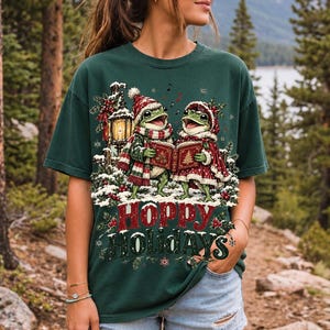 Two frogs singing carols in the snow with a lantern and songbook, text Hoppy Holidays