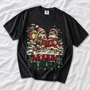 Two frogs singing carols in the snow with a lantern and songbook, text Hoppy Holidays