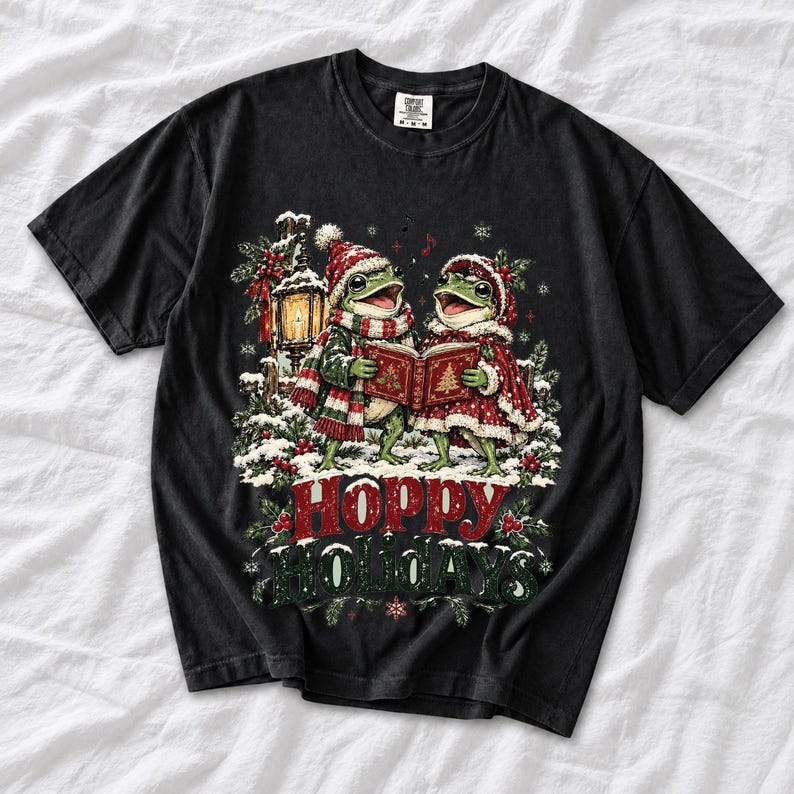 Two frogs singing carols in the snow with a lantern and songbook, text Hoppy Holidays