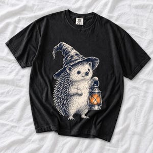 Etched pen illustration of a hedgehog in a witch hat holding a lantern, bone white with orange accent