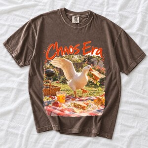 Goose stealing a sandwich from a picnic blanket, 90s film photo style, text "Chaos Era"