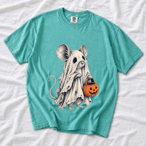 Etched pen illustration of a small mouse in a sheet ghost costume holding a candy bucket, bone white with orange accent