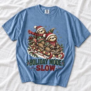 Two sloths in ugly sweaters riding a sled with lights and the text Holiday Mode: Slow