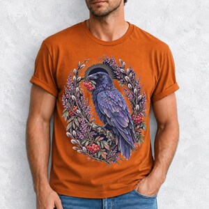 Raven holding a rowan berry inside an oval wreath of heather and catkins, painted cottagecore bird illustration