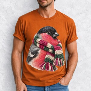 Colored-pencil bullfinch bird wrapped in a chunky striped knit scarf, cozy winter birdwatcher t-shirt art