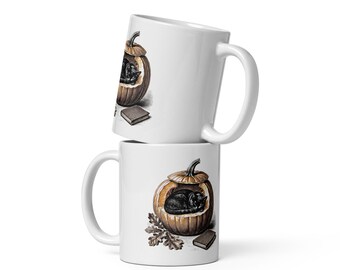 May include: Two white ceramic mugs stacked vertically. Each mug features a detailed illustration of a black cat curled up inside a hollowed-out orange pumpkin, accompanied by a small brown book and a cluster of brown oak leaves at the base.