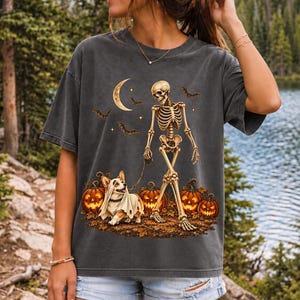 A skeleton walking a corgi in a ghost costume past carved pumpkins under a crescent moon