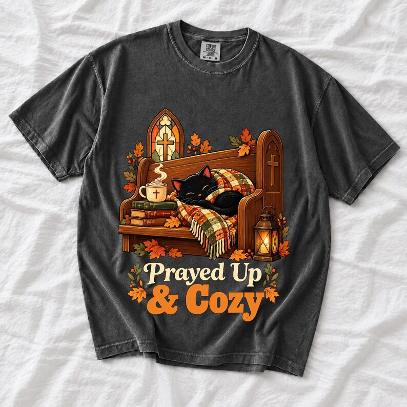Black cat curled on a church pew with blanket and cocoa among autumn leaves, text "Prayed Up & Cozy", retro illustration