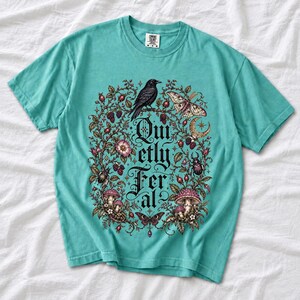 Raven on a wild rose branch with beetles and berries around blackletter text "Quietly Feral"