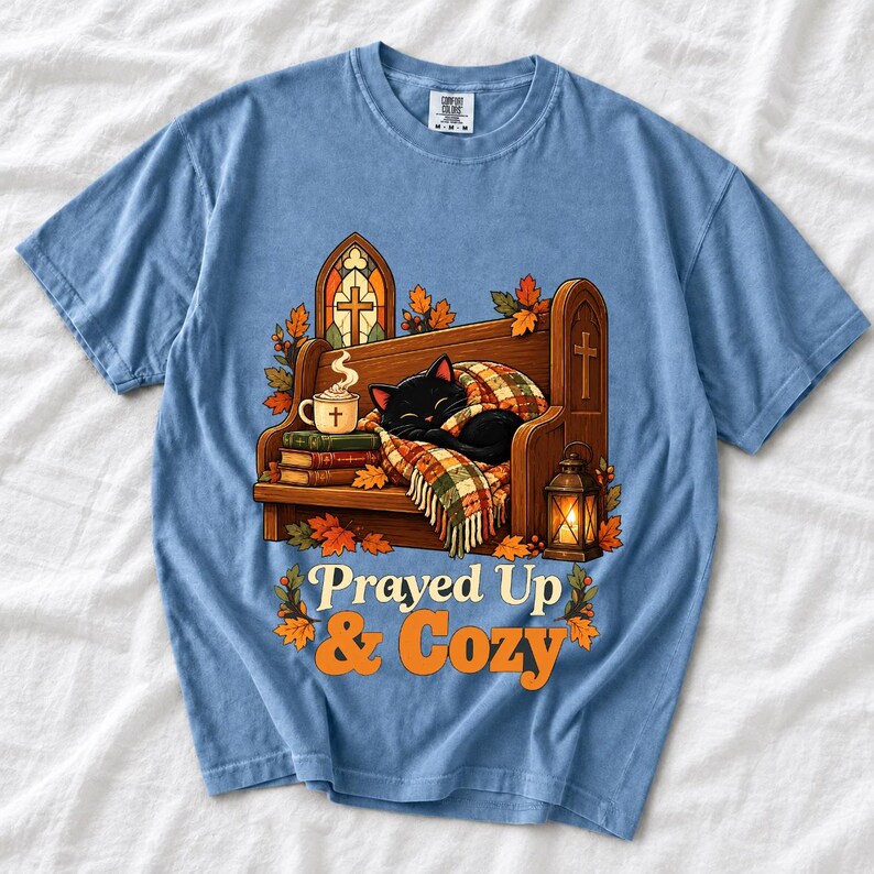 Black cat curled on a church pew with blanket and cocoa among autumn leaves, text "Prayed Up & Cozy", retro illustration