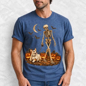 A skeleton walking a corgi in a ghost costume past carved pumpkins under a crescent moon