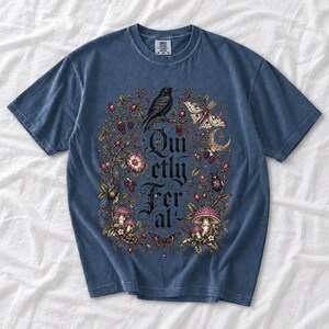 Raven on a wild rose branch with beetles and berries around blackletter text "Quietly Feral"